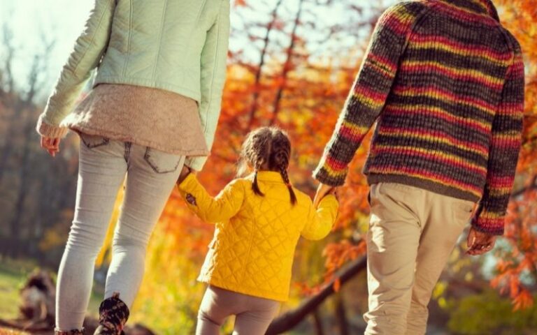 Mom and dad and little girl walking in the park in the fall time.